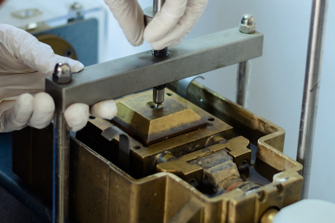 Gloved hands setting a specimen into a metal mould on a laboratory bench.