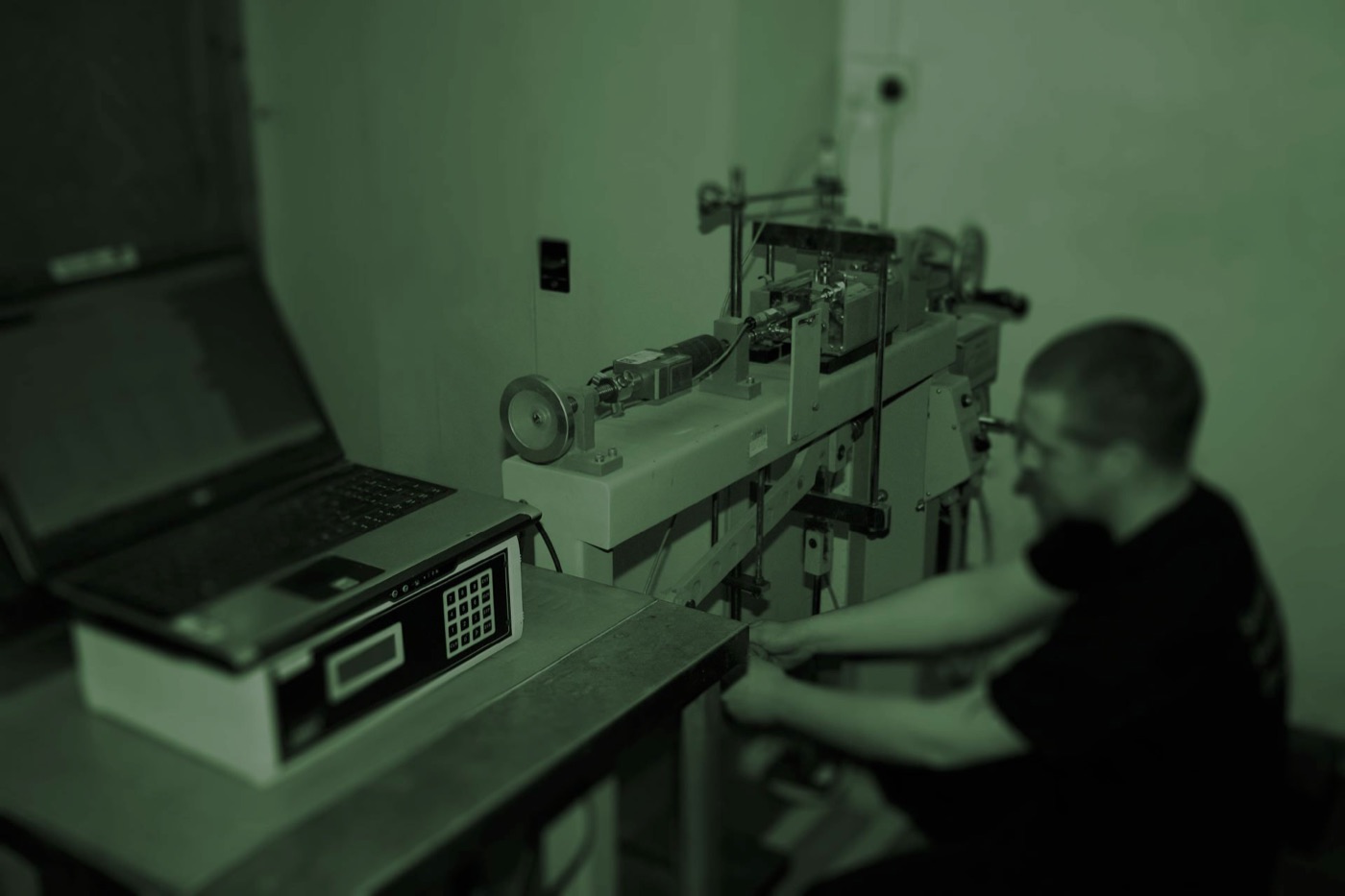 A technician at a bench-mounted test machine, with a laptop recording readings.